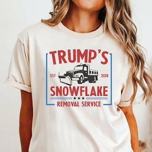 May include: A white t-shirt featuring a red and blue graphic design that reads "Trump's Snowflake Removal Service" with a black and white illustration of a snow plough truck. The text "EST 2024" is also included in the design.