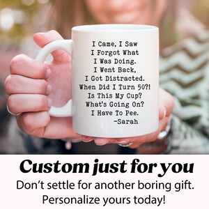 May include: White ceramic mug with a humorous poem about aging, including the text "I Came, I Saw, I Forgot What I Was Doing." The mug also includes the text "When Did I Turn 50?!" and "I Have To Pee." The mug is held by a person.