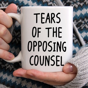 May include: White ceramic coffee mug with black text that reads "Tears of the Opposing Counsel".