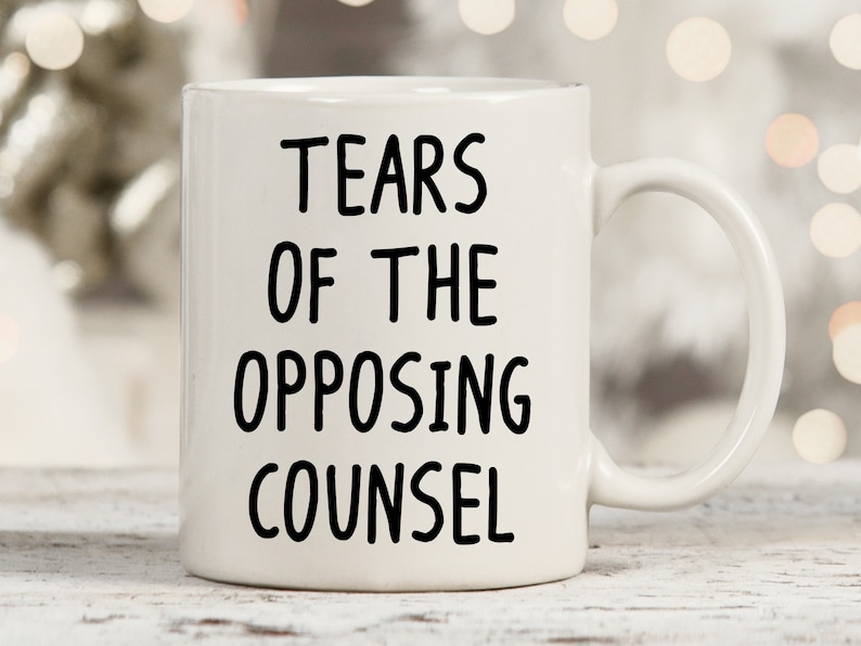 May include: White ceramic coffee mug with black text that reads "Tears of the Opposing Counsel".