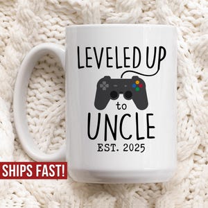 May include: White ceramic mug with a black and white design that says "LEVELED UP to UNCLE EST. 2025". A black and white video game controller is in the design.