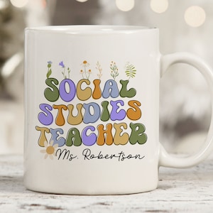 May include: White ceramic mug with a colorful retro design that says "Social Studies Teacher" with a floral design and the name "Ms. Robertson".