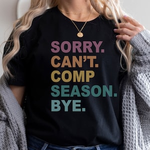 May include: Black t-shirt with a colorful graphic that reads "SORRY. CAN'T. COMP SEASON. BYE."
