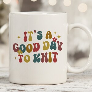 May include: White ceramic mug with a colorful retro design that says "It's a good day to knit".