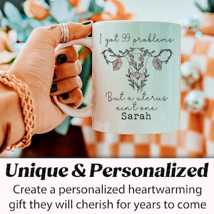 Pu&ograve; includere: Una tazza in ceramica bianca con un contorno nero di un utero con fiori e il testo "I got 99 problems But a uterus ain't one Sarah".