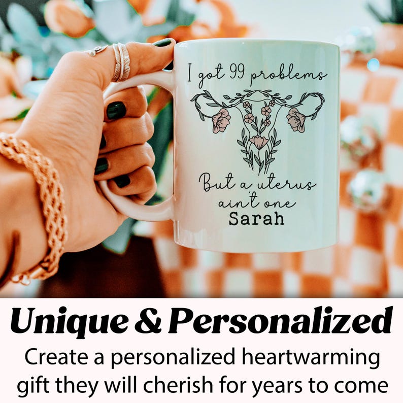 Pu&ograve; includere: Una tazza in ceramica bianca con un contorno nero di un utero con fiori e il testo "I got 99 problems But a uterus ain't one Sarah".