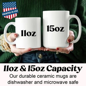 May include: Two white ceramic mugs, one labeled "11oz" and the other "15oz", are held in front of a green sweater. The mugs are part of a set, as indicated by the text "11oz & 15oz Capacity". The mugs are dishwasher and microwave safe.