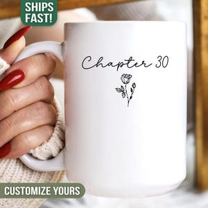 May include: White ceramic mug with the text "Chapter 30" in a handwritten font, accompanied by a small floral illustration. The mug has a large handle and is designed for hot beverages. The mug is a standard size.