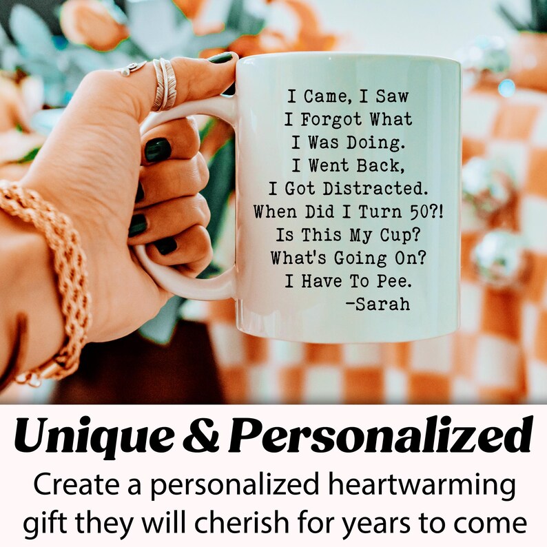 May include: A white ceramic mug with a black handle, featuring humorous text about aging and forgetfulness. The mug's text includes phrases like "I Came, I Saw, I Forgot What I Was Doing." The mug is held by a person.