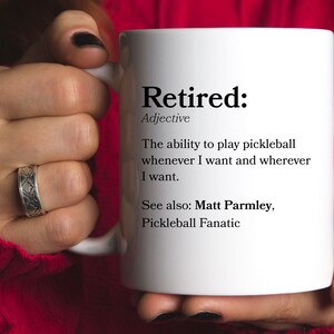 May include: White coffee mug with the word "Retired" defined as "The ability to play pickleball whenever I want and wherever I want."  The text also says "See also: Matt Parmley, Pickleball Fanatic."