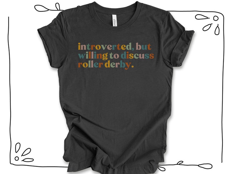 K&ouml;nnte beinhalten: Ein dunkelgraues T-Shirt mit dem Text "introvertiert, aber bereit, &uuml;ber Roller Derby zu diskutieren." in bunten Buchstaben.
