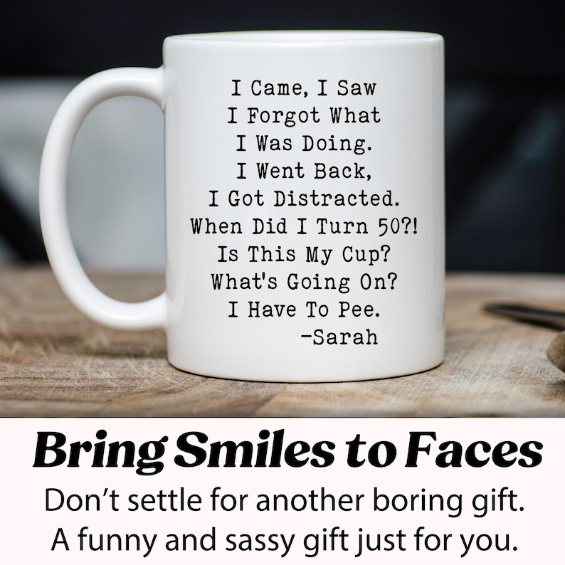 May include: White ceramic mug with a black humorous quote: "I Came, I Saw, I Forgot What I Was Doing..." and "I Have To Pee." The mug also includes the name "-Sarah." The mug is on a wooden surface. The bottom of the image says "Bring Smiles to Faces."