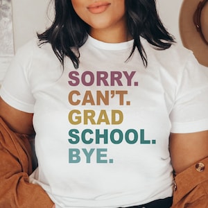 Może przedstawiać: Biała koszulka z napisem "SORRY. CAN'T. GRAD SCHOOL. BYE." w kolorowych literach.