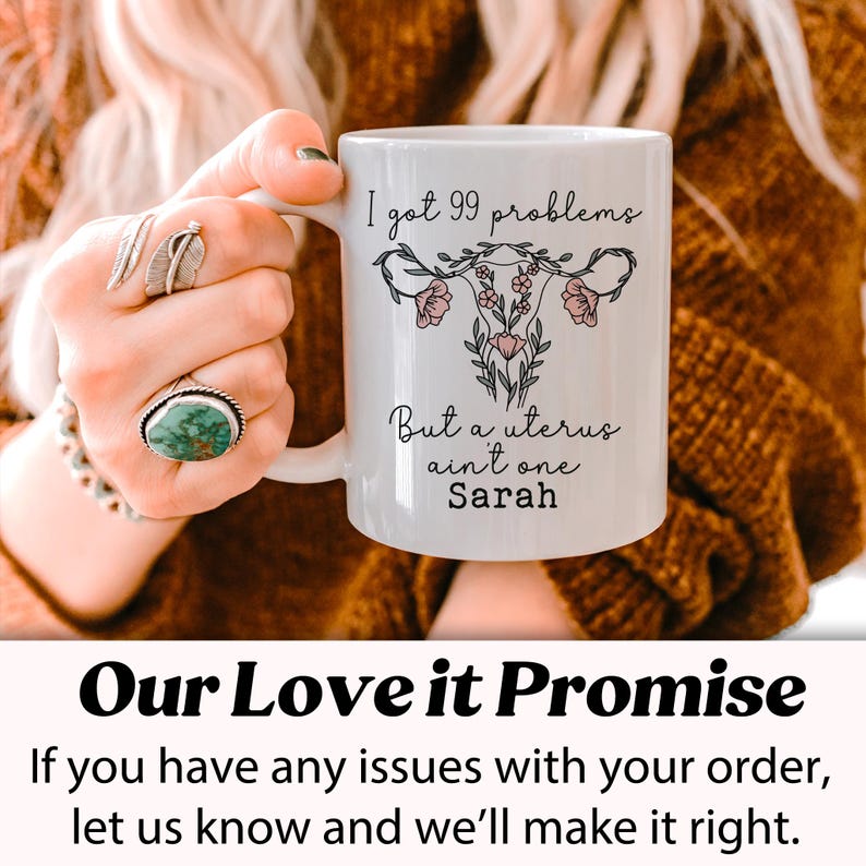 Pu&ograve; includere: Una tazza in ceramica bianca con una grafica nera e rosa di un utero con fiori e il testo "I got 99 problems But a uterus ain't one Sarah".