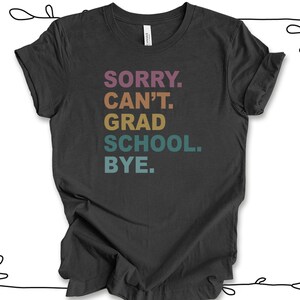 Może przedstawiać: Szary t-shirt z napisem "SORRY. CAN'T. GRAD SCHOOL. BYE." w kolorach tęczy.
