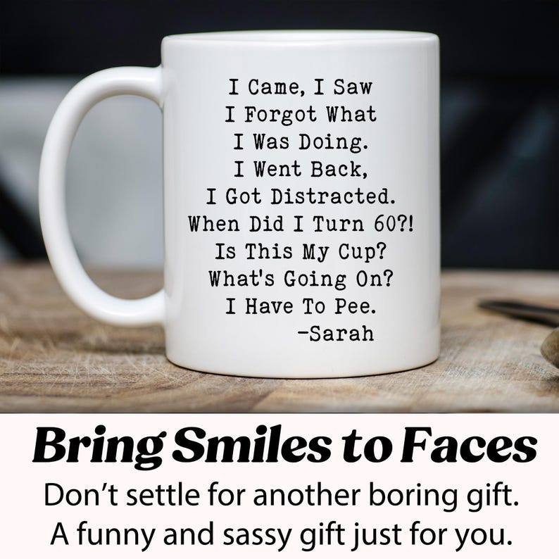 May include: White ceramic mug with a black humorous quote: "I Came, I Saw, I Forgot What I Was Doing..." and "When Did I Turn 60?!" The mug has a curved handle and is on a wooden surface. The text "Bring Smiles to Faces" is below the mug.