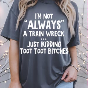 May include: Dark gray t-shirt with the text "I'M NOT 'ALWAYS' A TRAIN WRECK, ... JUST KIDDING TOOT TOOT BITCHES" in white. The shirt is a casual style, suitable for everyday wear.