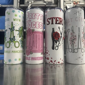 May include: Four white cylindrical tumblers featuring medical instrument graphics and text. The designs include surgical tools, flowers, butterflies, and the phrases "Pretty Process," "Sterile Processing," and "Certified Sterile Processing Technician."