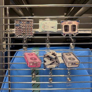 May include: Six acrylic badge reels featuring medical equipment designs. The top row shows a medication cart, a sterile surgical kit, and a crash cart. The bottom row displays a pink supply case, a tray with surgical tools, and a white supply case.