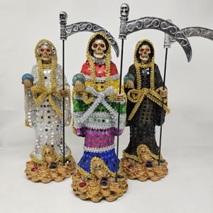 May include: Three skeletal figures, each holding a scythe, stand on a base of gold coins. The figures are dressed in different colors: one in white, one in rainbow colors, and one in black. Each figure has red eyes and a skull face.