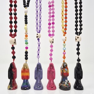 May include: Six hanging ornaments featuring a skeletal figure in a hooded robe, each suspended by a string of colorful beads. The beads include faceted glass, matte black, and white skull-shaped accents in red, purple, pink, and rainbow hues.