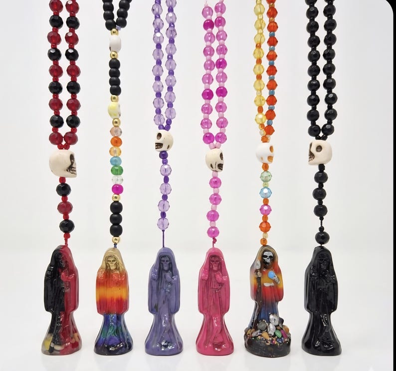 May include: Six hanging ornaments featuring a skeletal figure in a hooded robe, each suspended by a string of colorful beads. The beads include faceted glass, matte black, and white skull-shaped accents in red, purple, pink, and rainbow hues.