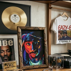 May include: A display of music memorabilia featuring a gold record, a framed Tupac portrait, a white Eazy-E t-shirt, and a Wu-Tang Clan cassette tape. The framed portrait has a wooden frame. The t-shirt has the words "EAZY-E" and "ETERNAL E" printed on it.