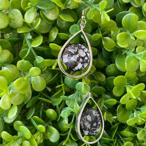 May include: A pair of silver teardrop earrings with black and white speckled stone accents.