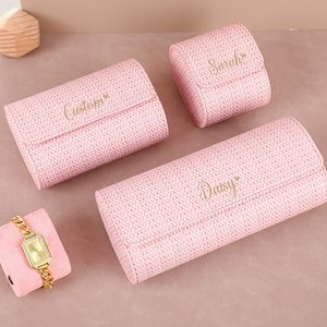 May include: Three pink jewellery boxes with woven fabric exteriors. The boxes are labelled "Custom", "Daisy", and "Sarah".