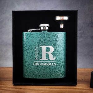 Pode incluir: Uma garrafa de metal verde com tampa e funil prateados. A garrafa é gravada com o texto "Randy Groomman" e a letra "R".