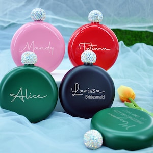 May include: Four personalised round metal hip flasks with a diamond-shaped stopper. The flasks are in pink, red, black, and green. The names "Mandy", "Tatiana", "Larissa Bridesmaid", and "Alice" are engraved on the flasks.