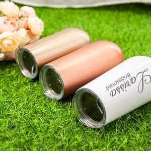 May include: Three personalized stainless steel tumblers with lids. The tumblers are in rose gold, copper, and white. The white tumbler has the text "Janessa bridesmaid" on it.