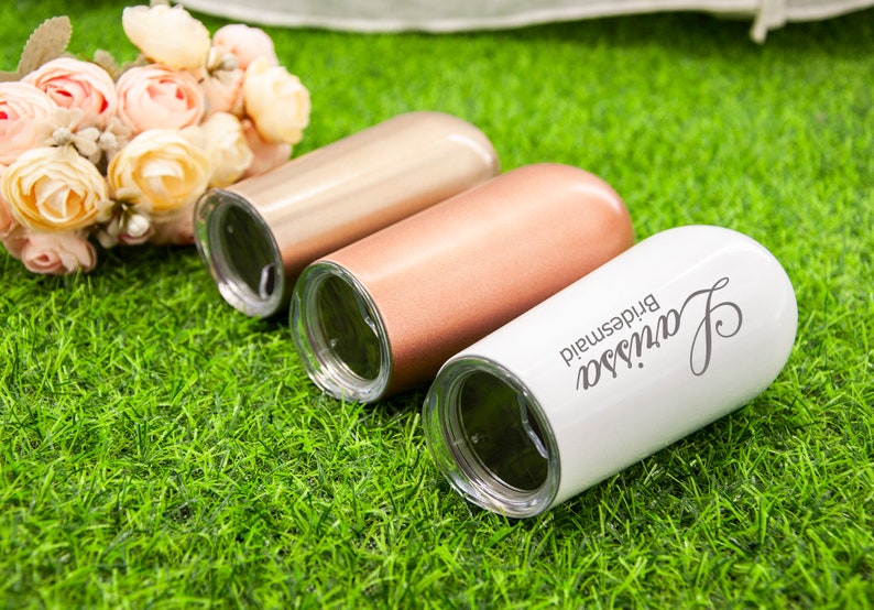May include: Three personalized stainless steel tumblers with lids. The tumblers are in rose gold, copper, and white. The white tumbler has the text "Janessa bridesmaid" on it.
