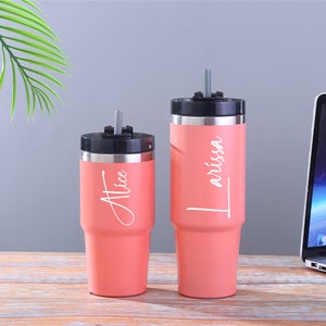 May include: Two pink stainless steel tumblers with lids and straws. The tumblers are personalized with the names "Alice" and "T'rissa".