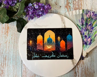 May include: A black and colorful jigsaw puzzle with a scene of a mosque at sunset. The puzzle features a crescent moon and stars, and the text "Ramadan Kareem Mubarak" in Arabic.