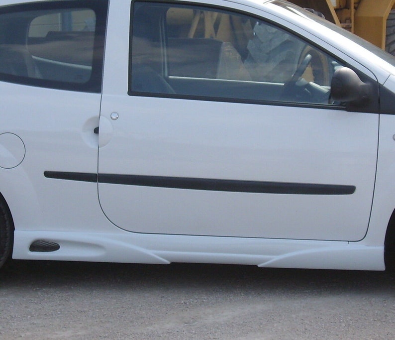 Puede incluir: Un coche blanco con molduras negras y un fald&oacute;n lateral. El coche tiene una manija de la puerta negra y un espejo lateral negro.