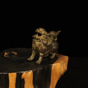 May include: A small, bronze statue of a mythical lion with intricate details. The statue is standing on a wooden base.