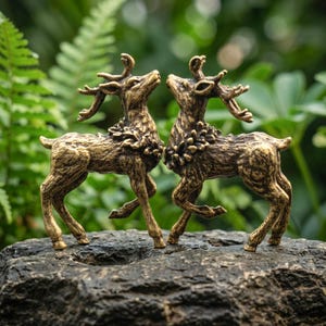 Op de afbeelding: Twee messingkleurige hertenbeeldjes die naast elkaar staan, elk met gedetailleerd gewei en een gestructureerde vacht. De herten staan tegenover elkaar met hun koppen omhoog gericht, met een metallic afwerking met donkere accenten.