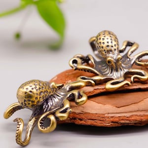 May include: Two antique brass octopus figurines. The octopuses have detailed textures and are posed on a piece of wood. The figurines have a vintage, weathered appearance, with a mix of gold and silver tones.