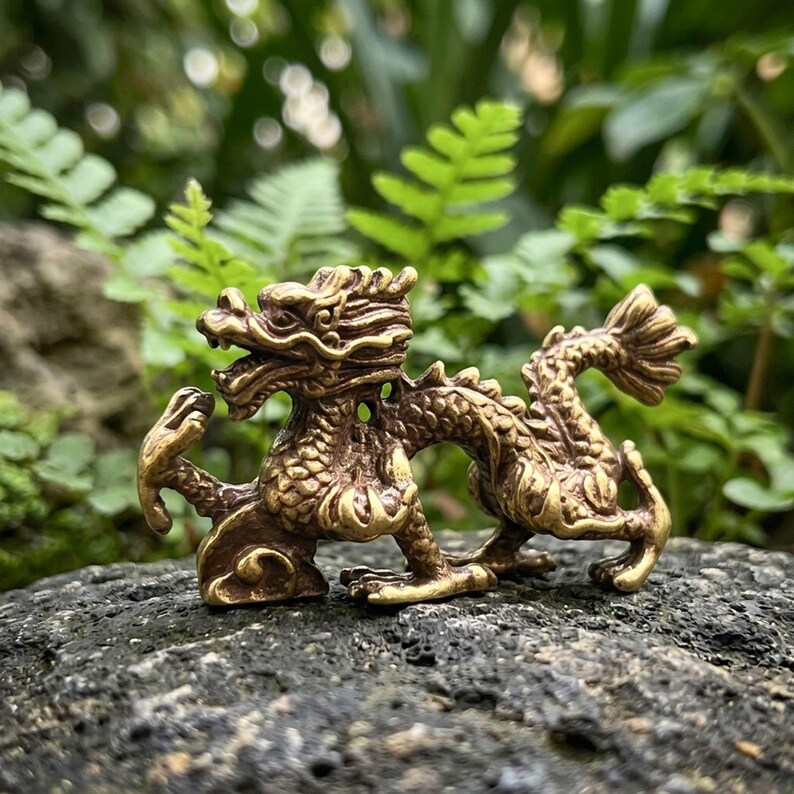 Puede incluir: Una peque&ntilde;a figura de drag&oacute;n de metal dorado con escamas intrincadas, una cabeza detallada con cuernos y un cuerpo largo y sinuoso. La criatura se muestra en una pose din&aacute;mica con las garras extendidas y la cola curvada, con un acabado pulido.