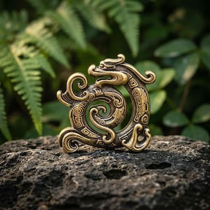 Può includere: Un ornamento metallico color ottone a forma di drago arrotolato con intricati motivi a spirale e incisioni geometriche. La figura del drago presenta un corpo curvo, una testa dettagliata con muso ed elementi della coda che si muovono in cerchio.