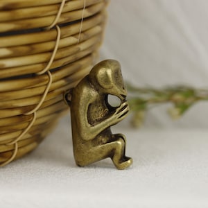 May include: A small, brass figurine of a person sitting with their head in their hands. The figurine is detailed and has a realistic appearance.