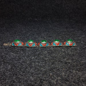 May include: A silver bracelet with five green cabochon stones set in ornate silver bezels. The bezels are decorated with red and blue enamel.