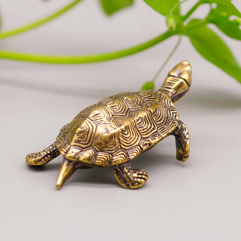 May include: A detailed, antique-style brass turtle figurine. The turtle has a textured shell with intricate patterns and is posed with its head and legs extended. The figurine is a warm, golden color, suggesting an aged finish.