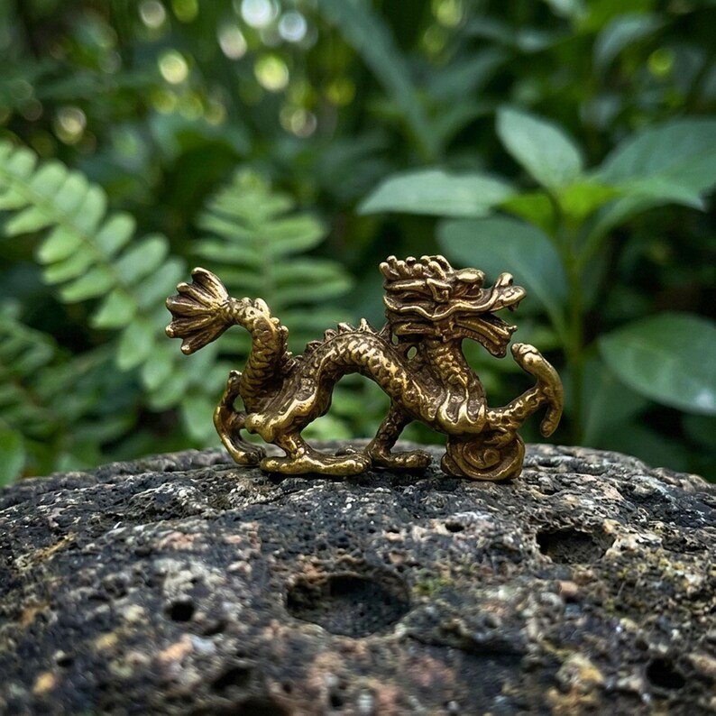 Puede incluir: Una peque&ntilde;a figura de drag&oacute;n de color oro met&aacute;lico con detalles intrincados de escamas, una cola curva y la boca abierta. El drag&oacute;n se muestra en una pose din&aacute;mica de caminata con el cuerpo arqueado y un acabado pulido.