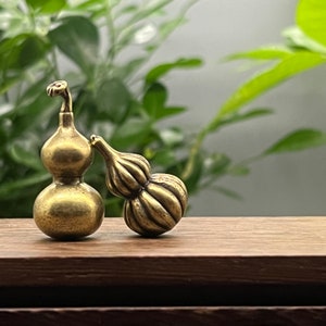 May include: Two small, gold-colored gourd-shaped ornaments. The ornament on the left has a round bottom and a smaller, round top. The ornament on the right is a single gourd shape.