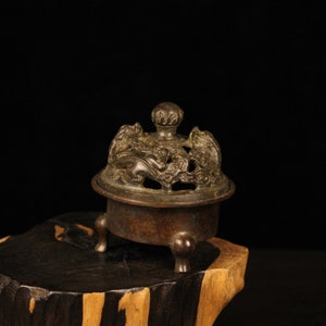 May include: A bronze incense burner with a decorative lid featuring intricate floral and animal motifs. The burner sits on three legs and has a circular base.