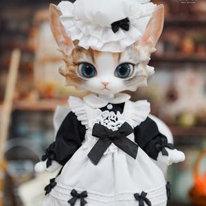 May include: A cat-faced doll in a white and black maid outfit, adorned with black bows. The doll features large blue eyes, a white bonnet, and a white apron with black trim. A unique collectible item.