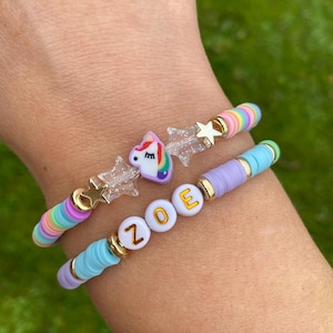 May include: Two colourful beaded bracelets with a unicorn charm and the name "ZOE" spelled out in white beads with gold lettering.