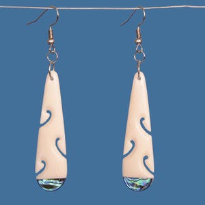 May include: A pair of white bone earrings with a carved design and abalone shell accents. The earrings are hanging from silver hooks.